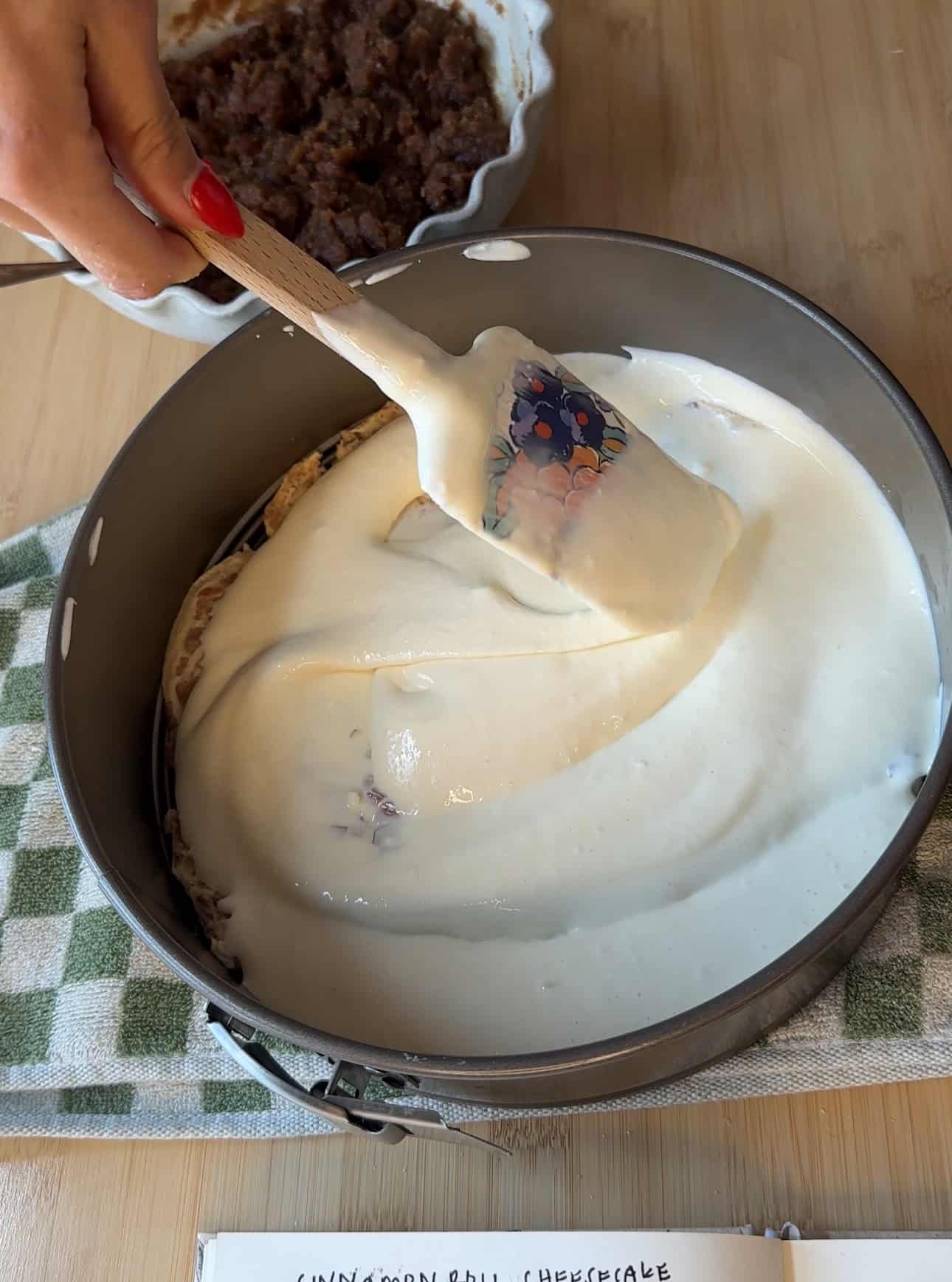 Smooth cheesecake batter being poured over the cinnamon roll crust.