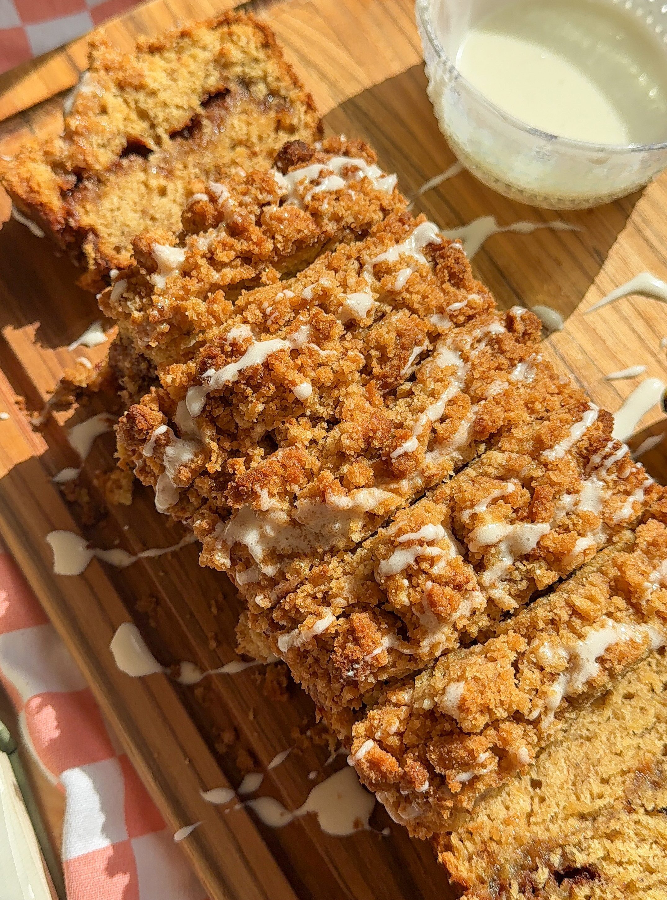 my cinnamon crunch banana bread sliced up on a cutting board next to the glaze and bananas