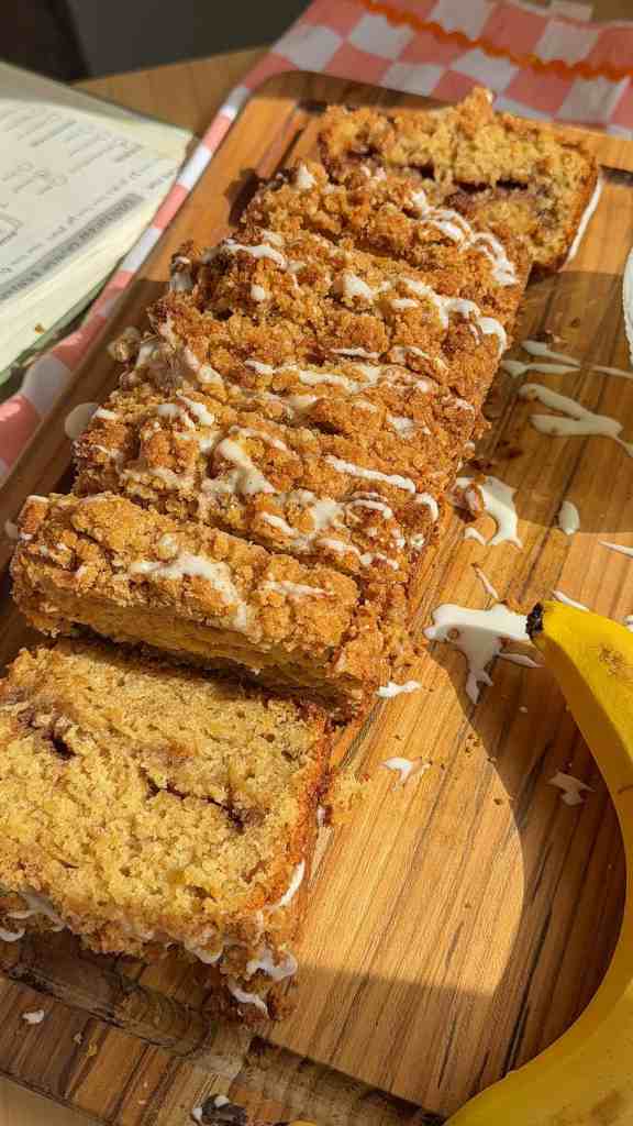 my cinnamon crunch banana bread sliced up on a cutting board next to the glaze and bananas