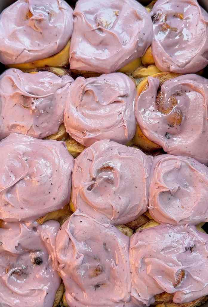 a close up of all of my blueberry cinnamon rolls in a pan with fresh blueberry cream cheese frosting