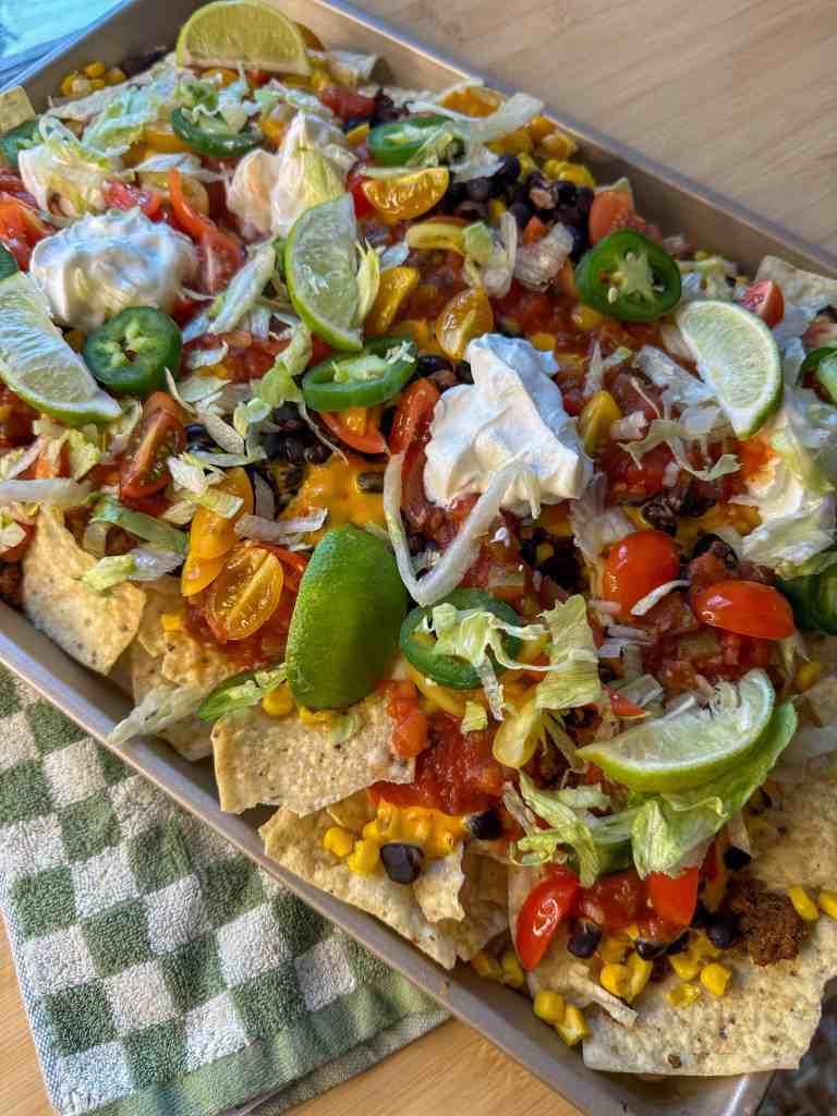 a final image of my sheet pan nachos fresh oit of the oven with all of the cold toppings, ready to be enjoyed by my family!