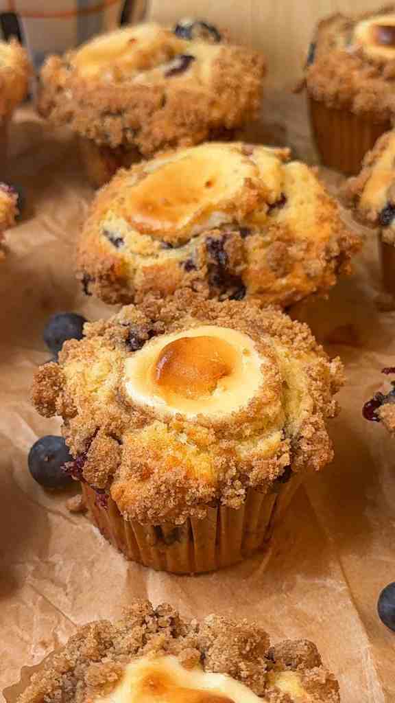 a close up of my cheesecake stuffed blueberry crumble muffins on parchment paper